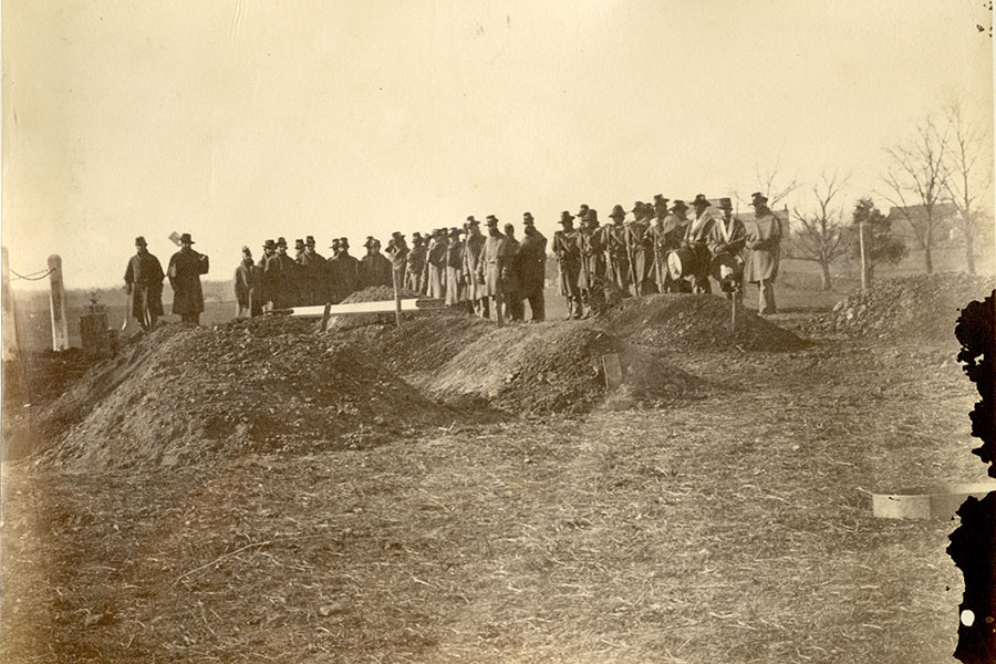 a black and white photo of man standing at the burial place at camp griffin