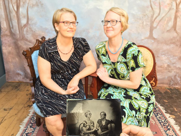 Two women sit close posing for their tintypes, featured in the foreground. 